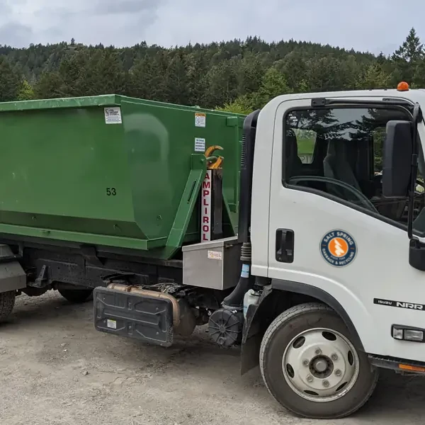 Roll-off truck with a green bin at the yard