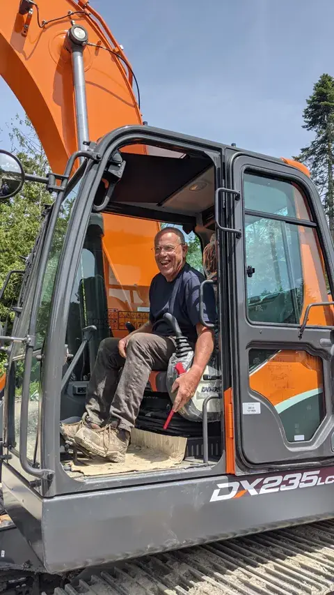 Mike, a longtime Salt Spring Garbage employee, smiling in the cab of the company's new orange Doosan excavator