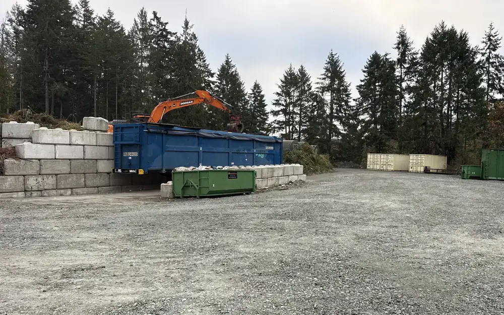Salt Spring Island transfer station drop-off yard with an orange excavator loading a blue bin, and green rental bins